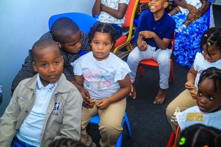 A high-angle view of children seated close together, a boy in a beige jacket in the foreground and a girl in a white T-shirt beside him.